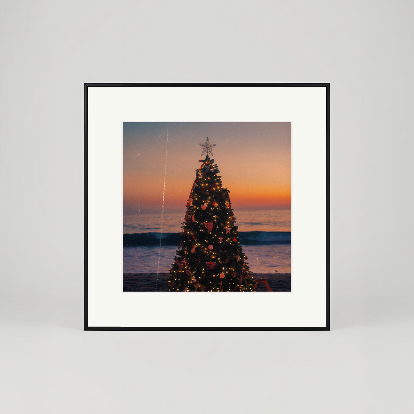 Framed artwork of a Christmas tree on a beach at sunset.