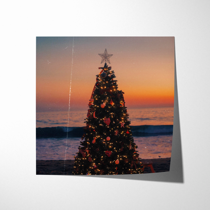 Decorated Christmas tree on a beach at sunset with ocean waves in the background.