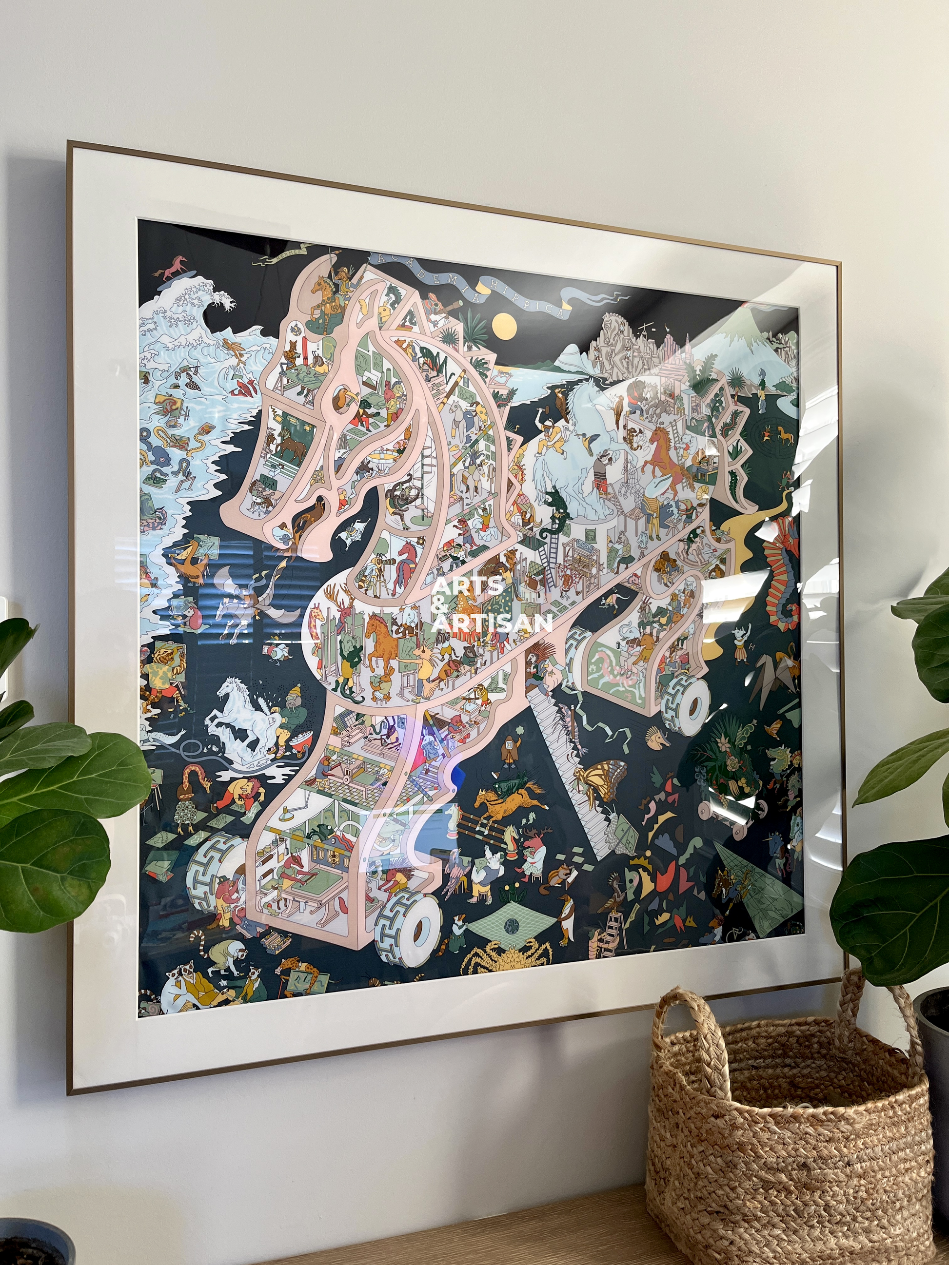 Framed artwork of a scarf frame, Hermes scarf frame on a wall with plants and a basket below.