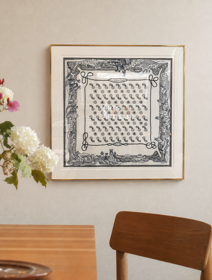 Framed hermes scarf frame on a wall with a wooden table and chair in the foreground