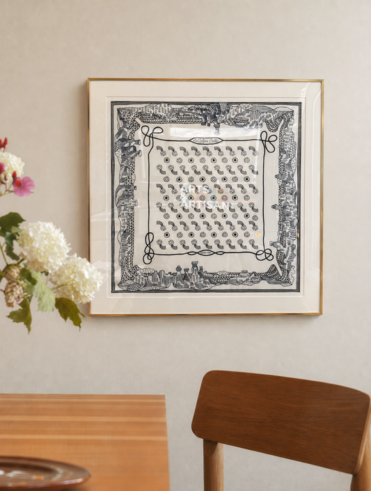Framed hermes scarf frame on a wall with a wooden table and chair in the foreground