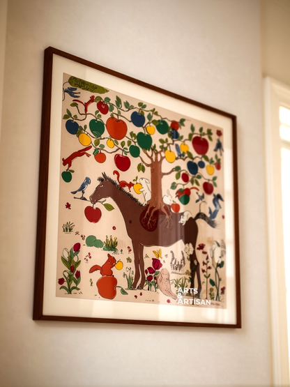 A framed art print featuring a whimsical illustration of a brown horse under a tree of colorful apples, hanging on a beige wall.