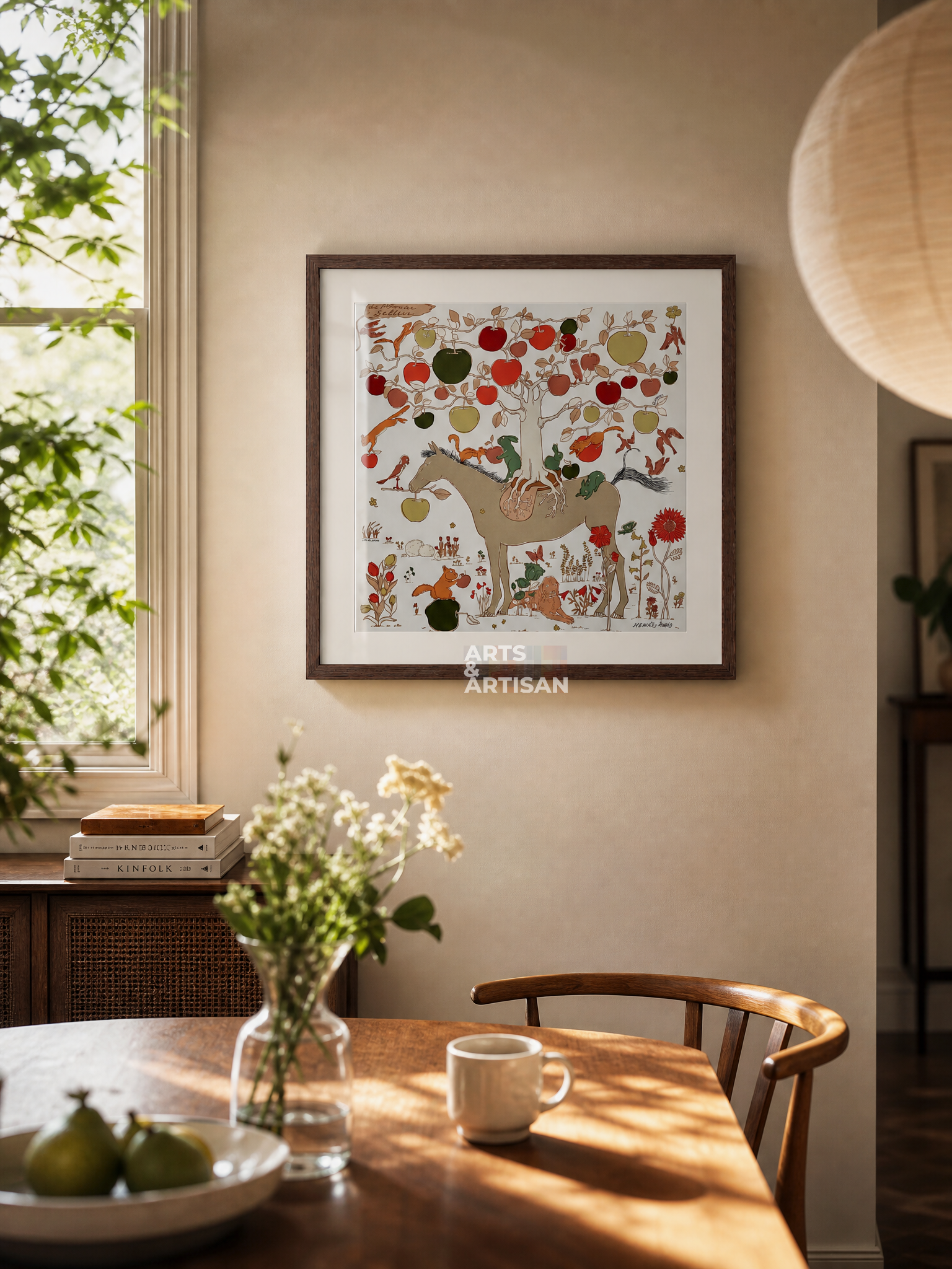 A framed Hermes Scarf 45 featuring a whimsical forest scene with a deer, trees, and colorful fruits, displayed on a beige wall in a warm, sunlit dining room setting.