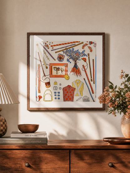 A framed Hermes Scarf 70 featuring a colorful collage of sewing and fashion-themed illustrations, displayed on a beige wall above a wooden console table with a lamp, books, and flowers.