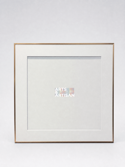 A square picture frame with a white mat and a thin gold-toned metal border, shown against a light gray studio background. A small Arts & Artisan logo is visible in the center of the mat.