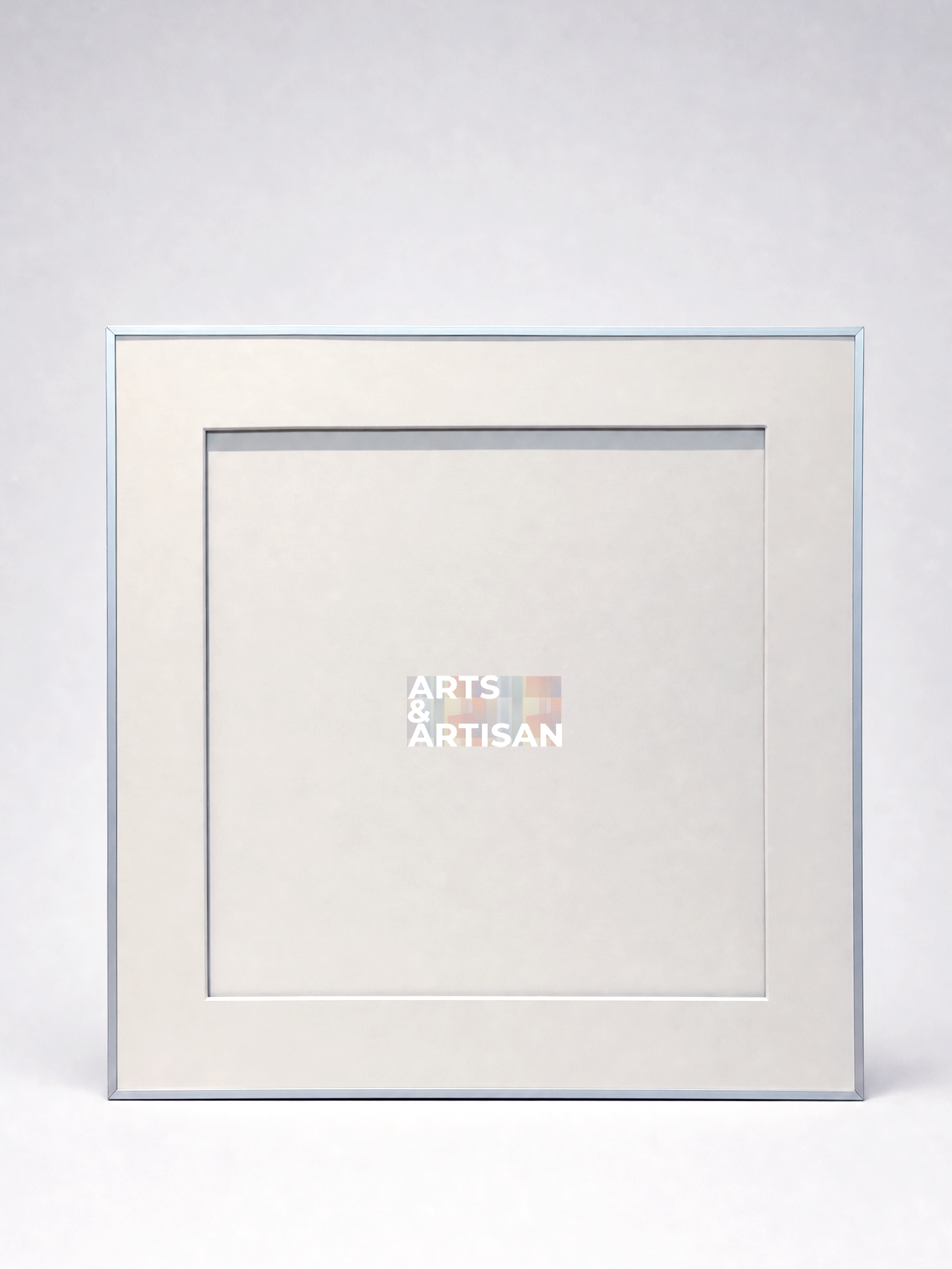 A square picture frame with a light beige mat and a thin silver-toned border, shown against a light gray background. The center of the mat features a small logo that reads 'ARTS & ARTISAN'.