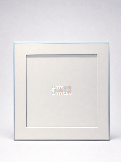 A square picture frame with a light beige mat and a thin silver-toned border, shown against a light gray background. The center of the mat features a small logo that reads 'ARTS & ARTISAN'.
